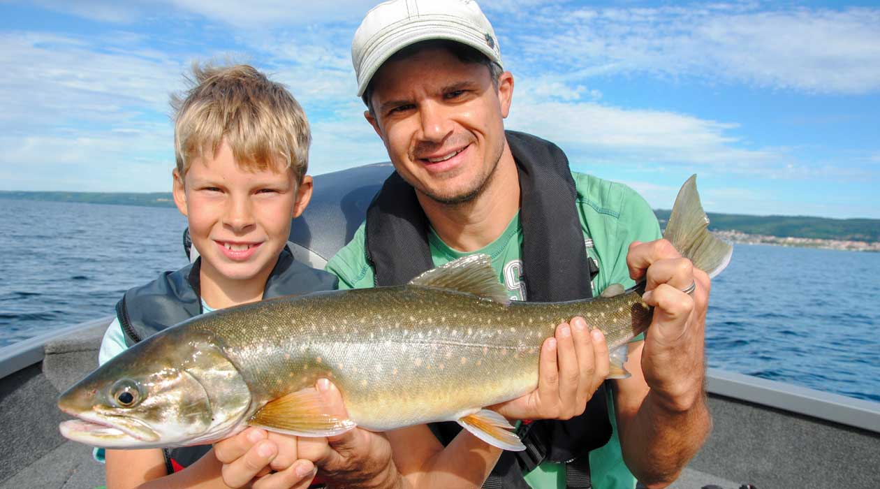 Mann und ein Junge halten einen grossen Fisch im Ruderboot auf einem See