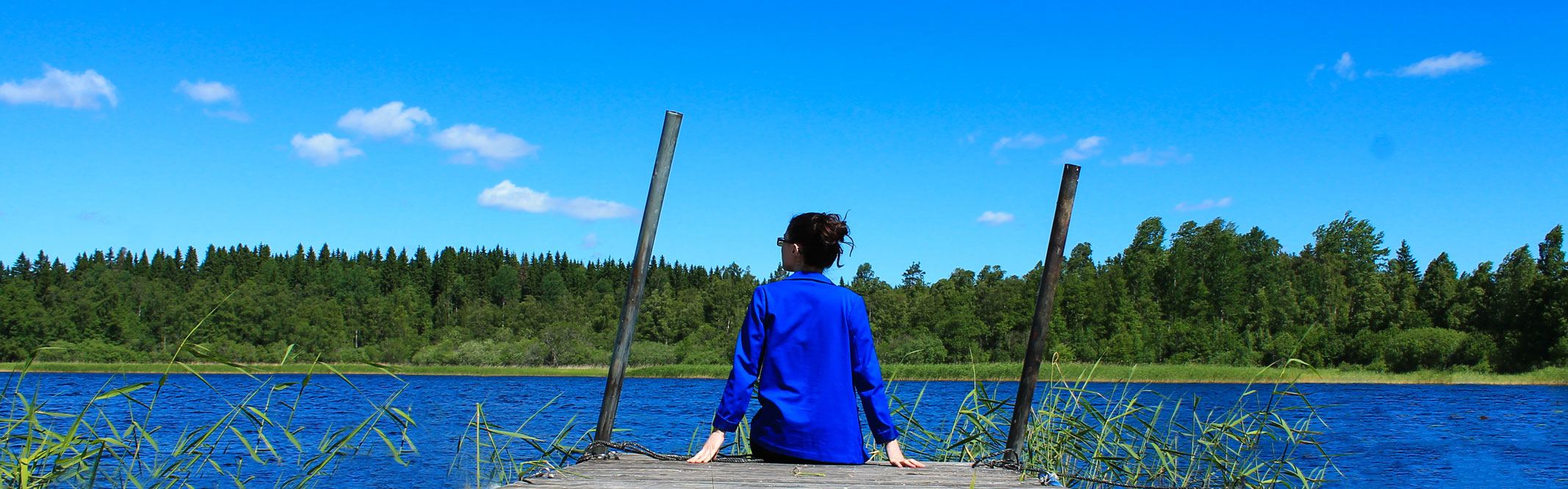Kvinna sitter på en brygga och tittar över en sjö.