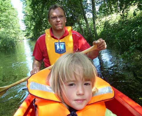Vater und Kind sitzen in einem Kanu und haben gelbe Rettungswesten an