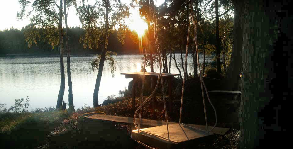 Solen håller på att gå ner och skiner över en sjö på en gunga